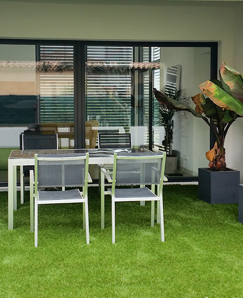 Table, chaises et pots de fleurs posés sur une terrasse en gazon artificiel